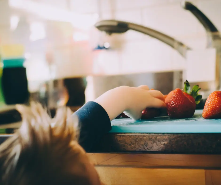 A child try to take a strawberry from the table