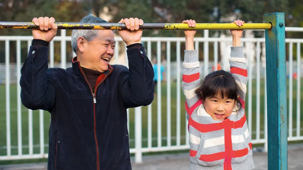 Elderly man and grandchild hanging on a monkey bar in a playground