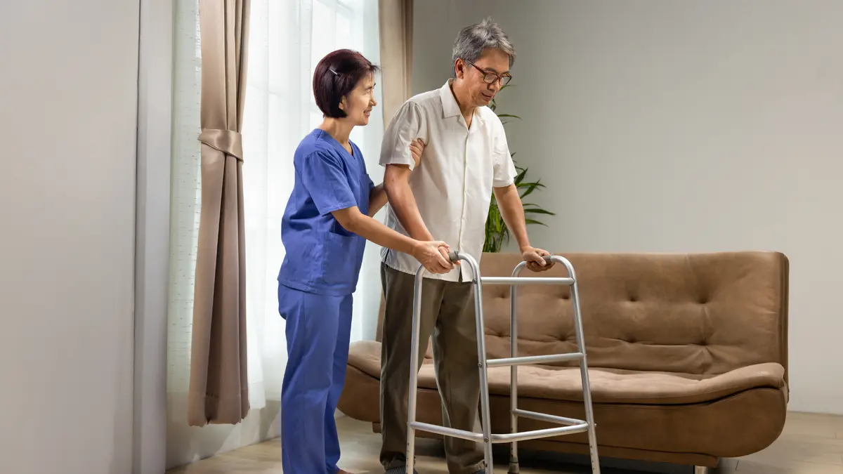Nurse assisting an elderly Asian man to walk